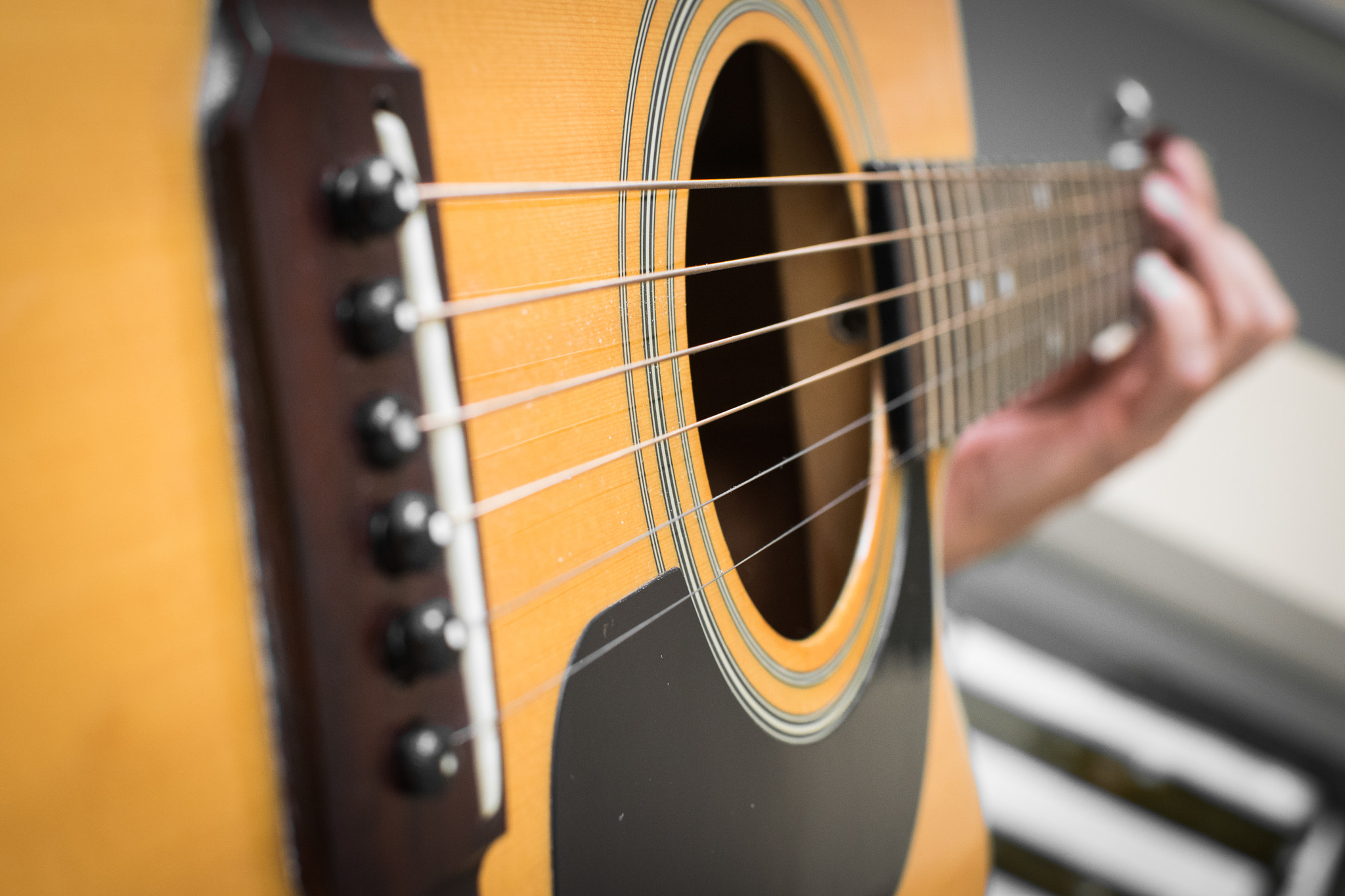 Close view of an acoustic guitar and a player’s fretting hand